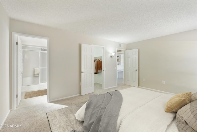 bedroom with light carpet, a walk in closet, ensuite bath, a textured ceiling, and a closet