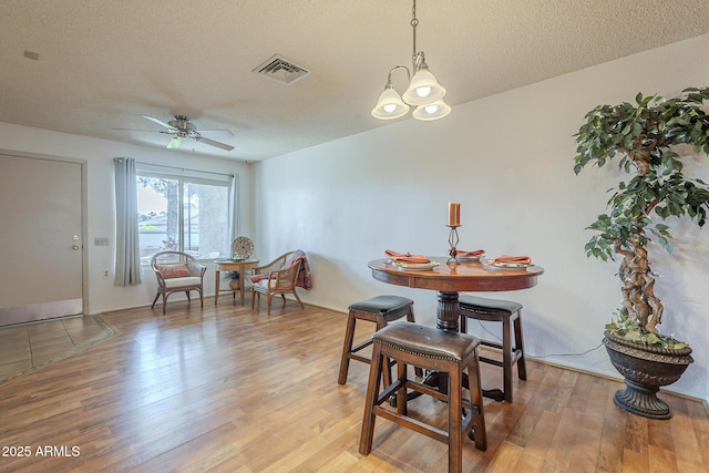 dining area with hardwood / wood-style flooring, ceiling fan with notable chandelier, and a textured ceiling