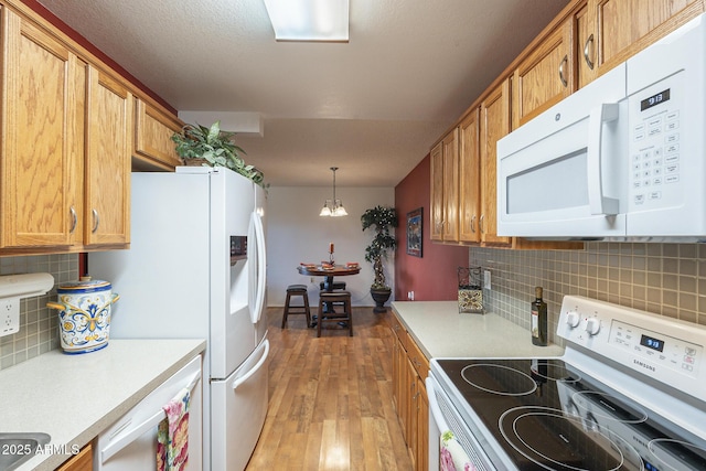 kitchen featuring tasteful backsplash, an inviting chandelier, decorative light fixtures, light wood-type flooring, and white appliances