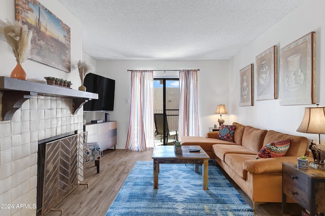 living area with a tiled fireplace, light wood-type flooring, and a textured ceiling