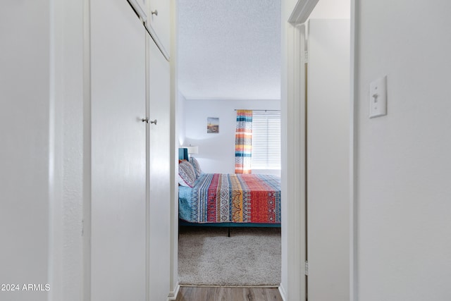 corridor with light wood-type flooring and a textured ceiling