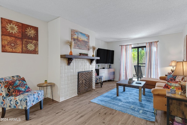 living room with baseboards, a tile fireplace, light wood-style floors, and a textured ceiling