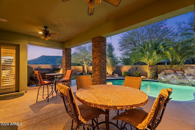 patio terrace at dusk with a fenced in pool, ceiling fan, and a mountain view