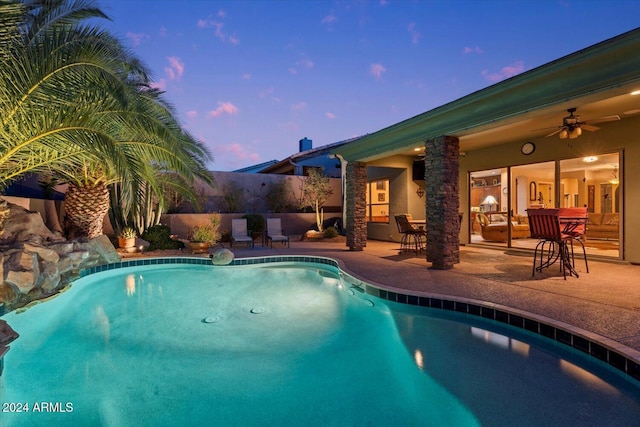 pool at dusk featuring ceiling fan and a patio