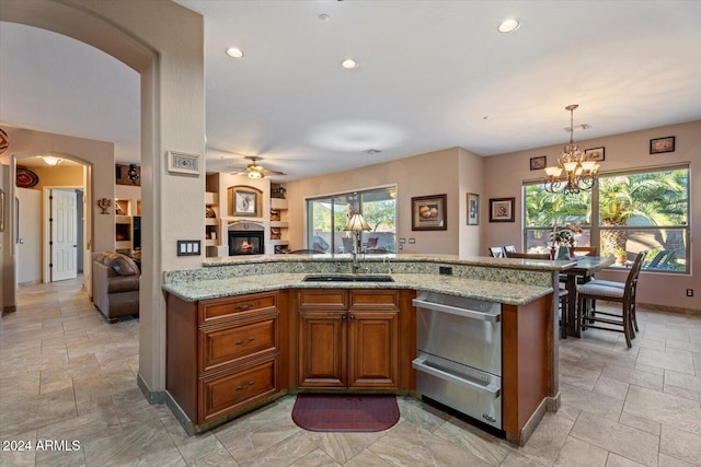 kitchen featuring a wealth of natural light, light stone counters, sink, and hanging light fixtures