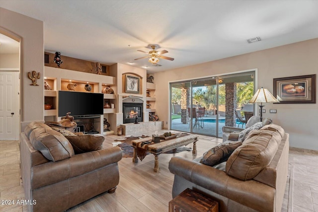 living room with built in shelves, ceiling fan, and light hardwood / wood-style floors