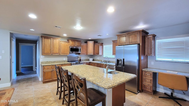 5539 E Dragoon Ave, Mesa, AZ 85206 - kitchen with appliances with stainless steel finishes, a kitchen island with sink, light stone counters, brown cabinetry, and recessed lighting