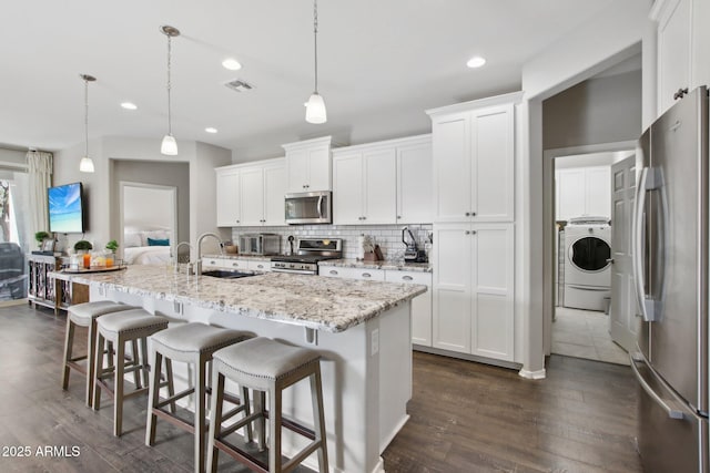 kitchen with hanging light fixtures, washer / dryer, a center island with sink, and appliances with stainless steel finishes