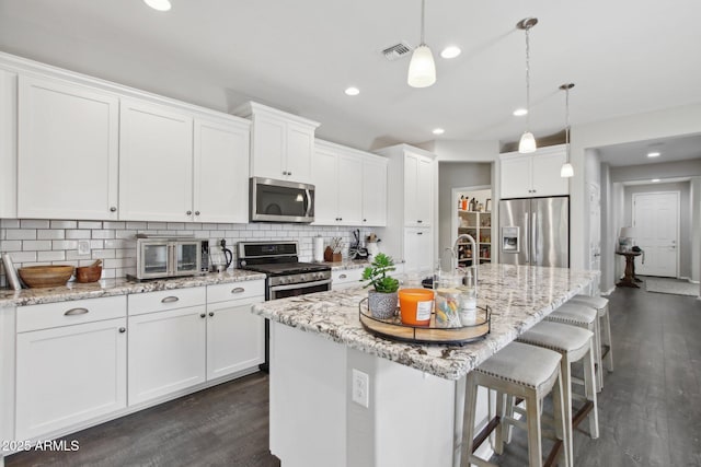 kitchen with stainless steel appliances, decorative light fixtures, an island with sink, and white cabinets