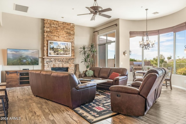 living room with ceiling fan with notable chandelier, light wood-type flooring, and a stone fireplace