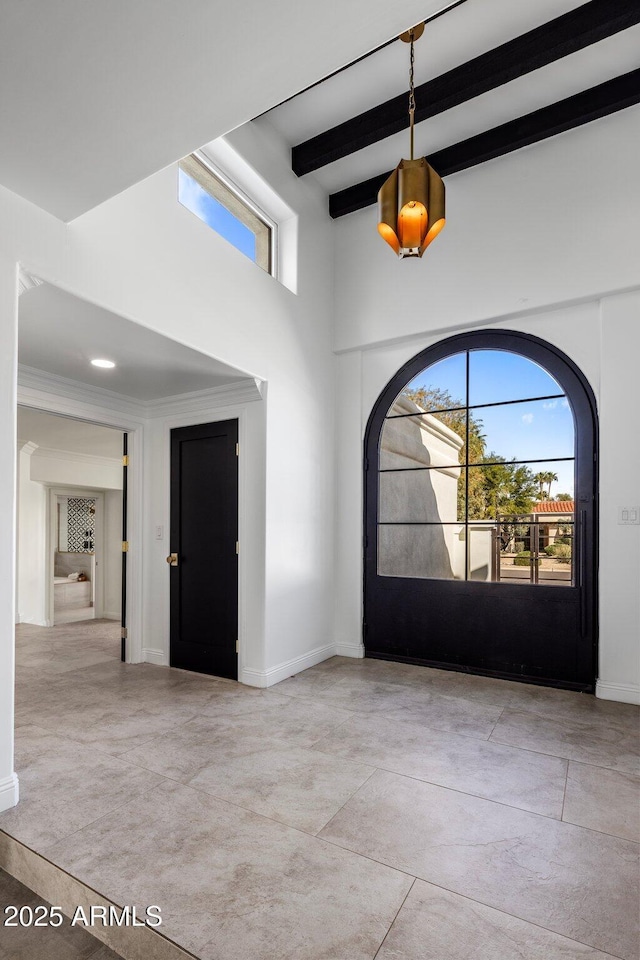 foyer entrance with beam ceiling, a high ceiling, baseboards, and ornamental molding