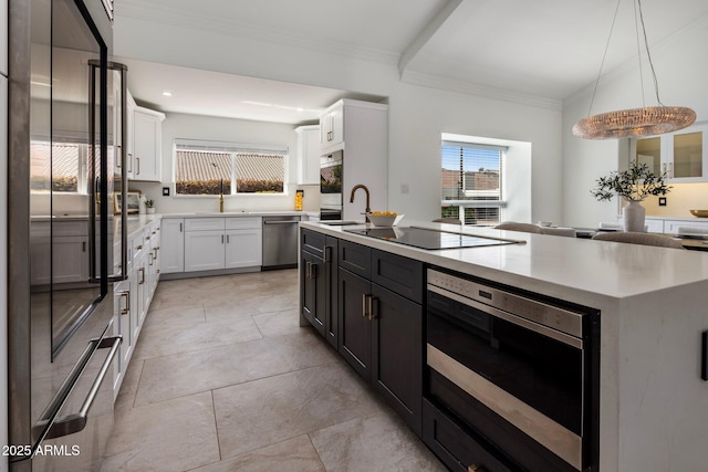 kitchen featuring a kitchen island with sink, a sink, white cabinets, appliances with stainless steel finishes, and crown molding