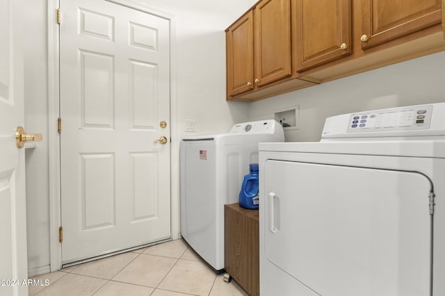 washroom featuring washing machine and dryer, cabinets, and light tile patterned floors