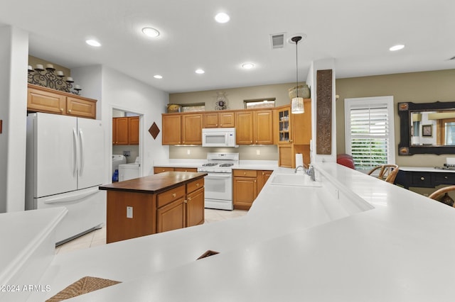 kitchen with light tile patterned flooring, sink, kitchen peninsula, hanging light fixtures, and white appliances