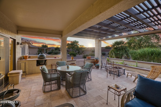 patio terrace at dusk featuring an outdoor kitchen and a pergola