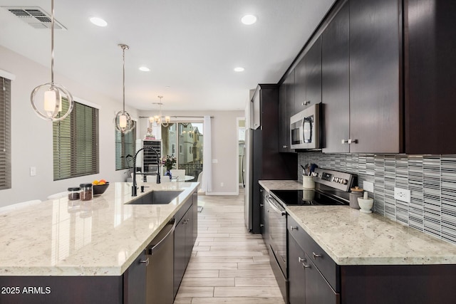 kitchen featuring visible vents, decorative backsplash, appliances with stainless steel finishes, a large island with sink, and a sink