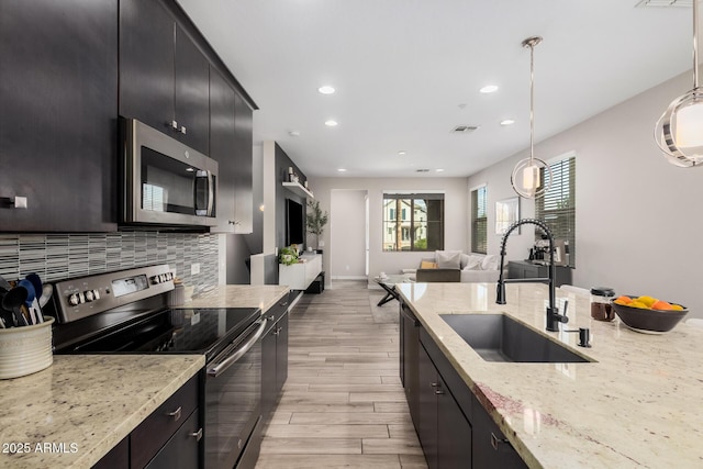 kitchen featuring stainless steel appliances, decorative backsplash, a sink, and dark cabinets