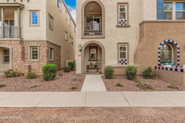 view of exterior entry with a balcony, stone siding, and stucco siding