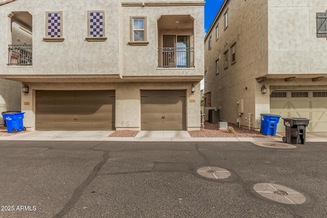 view of front of home with central air condition unit, an attached garage, a balcony, and stucco siding