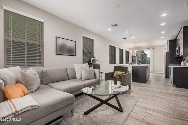 living room with light wood-style floors, recessed lighting, visible vents, and an inviting chandelier