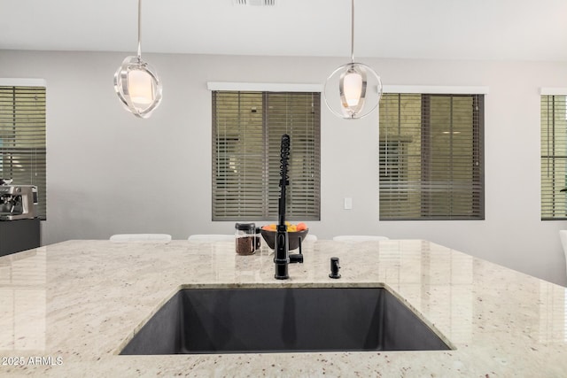 kitchen featuring hanging light fixtures, light stone countertops, and a sink