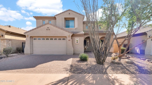 mediterranean / spanish-style home with a garage, decorative driveway, a tile roof, and stucco siding