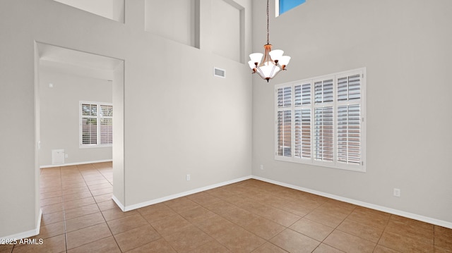 tiled spare room with baseboards, a towering ceiling, visible vents, and a notable chandelier
