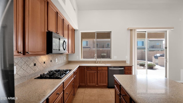 kitchen with black gas cooktop, a sink, stainless steel dishwasher, brown cabinets, and tasteful backsplash