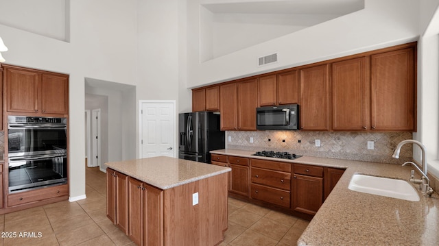 kitchen with visible vents, brown cabinetry, a center island, black appliances, and a sink