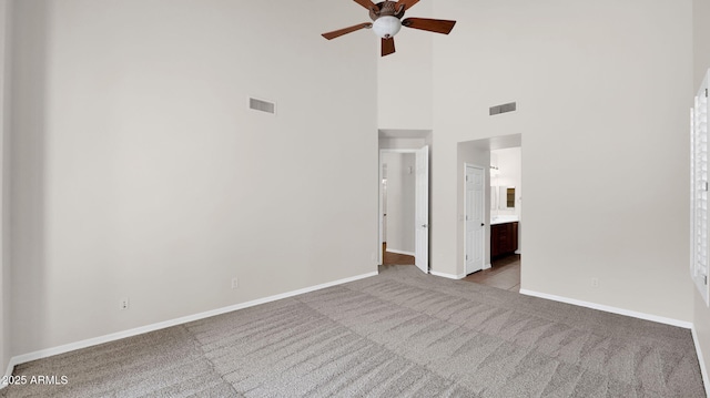 unfurnished bedroom featuring carpet, visible vents, a towering ceiling, ensuite bathroom, and baseboards