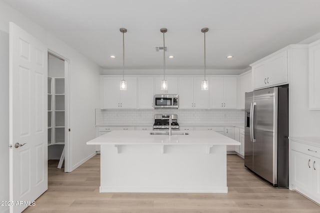 kitchen with a center island with sink, white cabinets, stainless steel appliances, and decorative light fixtures