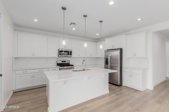 kitchen featuring stainless steel appliances, sink, pendant lighting, a center island with sink, and white cabinets