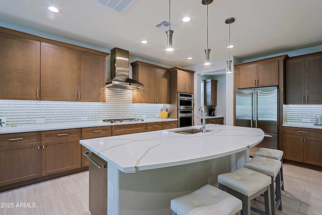 kitchen with pendant lighting, wall chimney range hood, sink, stainless steel appliances, and tasteful backsplash