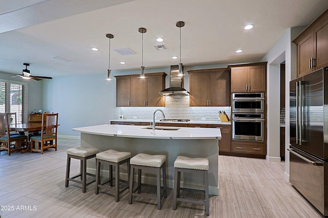 kitchen featuring appliances with stainless steel finishes, sink, an island with sink, and wall chimney range hood