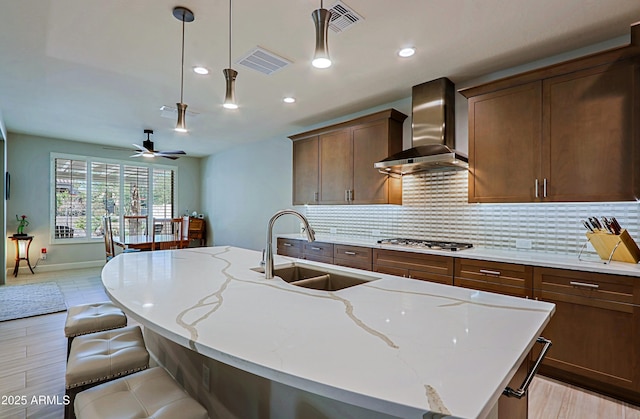 kitchen with a kitchen island with sink, sink, light stone counters, and wall chimney exhaust hood