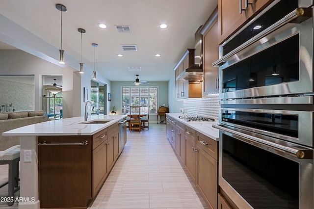 kitchen with appliances with stainless steel finishes, decorative light fixtures, sink, decorative backsplash, and a center island with sink