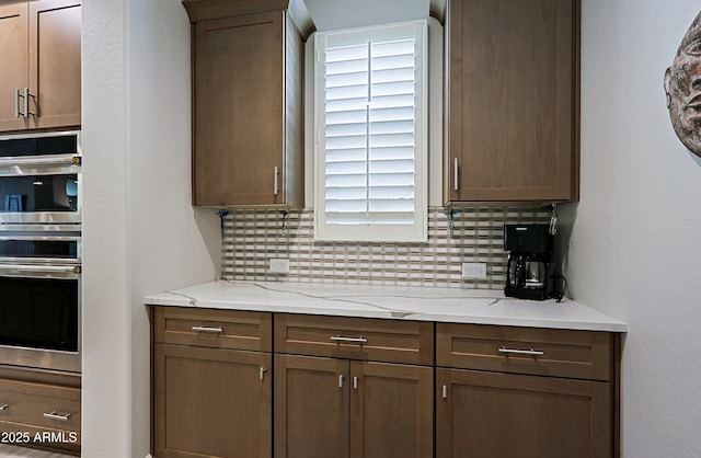 kitchen featuring light stone counters, double oven, and decorative backsplash