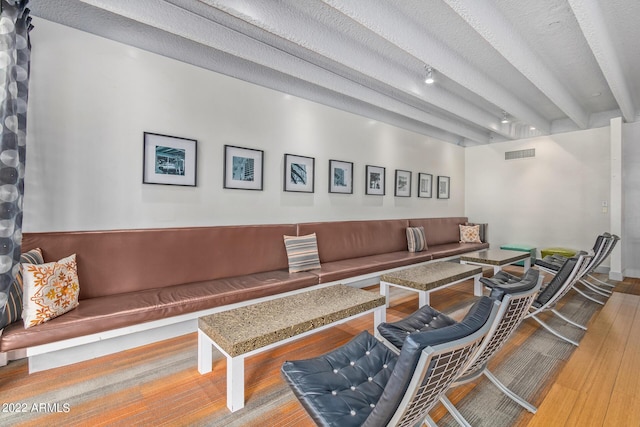 living room with beam ceiling, visible vents, a textured ceiling, and wood finished floors