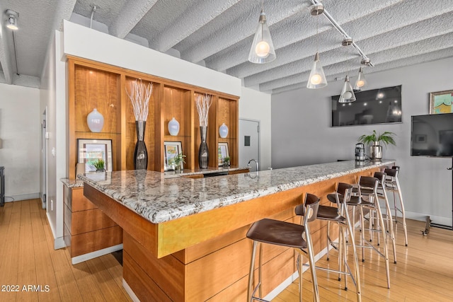 bar with light wood-type flooring, indoor wet bar, hanging light fixtures, and baseboards