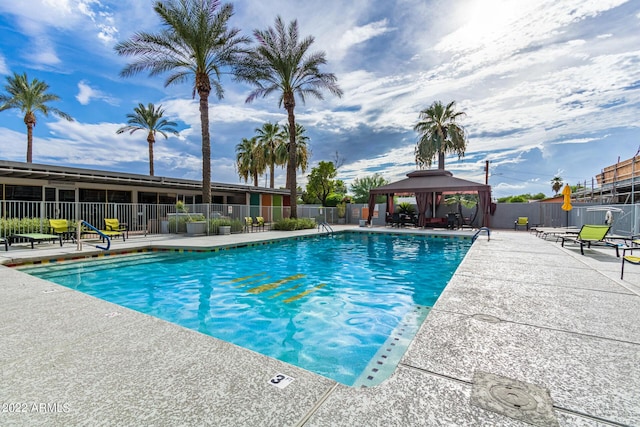 community pool with a patio area, fence, and a gazebo