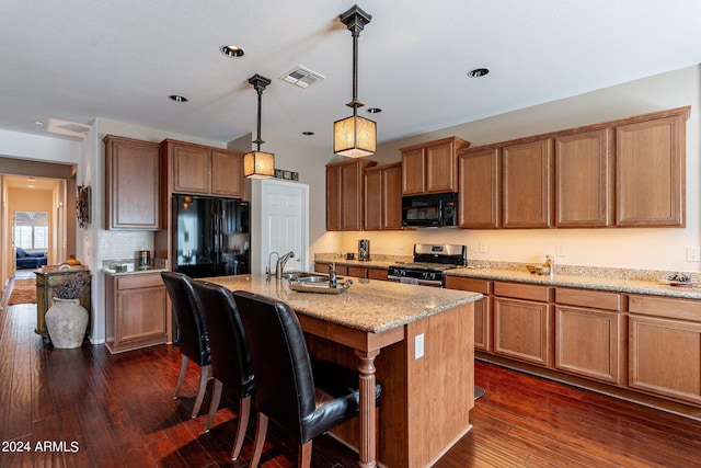 kitchen featuring decorative light fixtures, light stone countertops, dark wood-type flooring, black appliances, and an island with sink