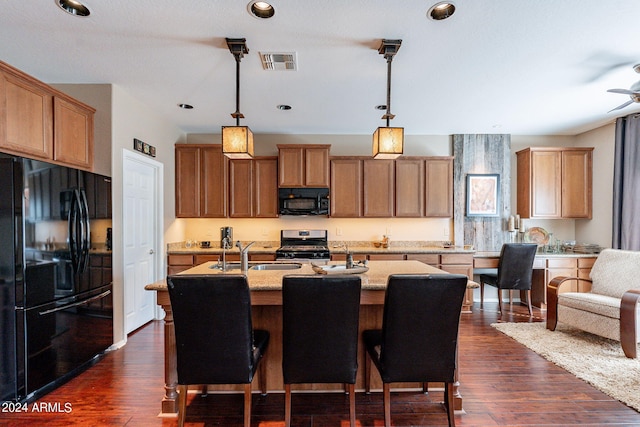 kitchen featuring pendant lighting, a kitchen island with sink, dark wood-type flooring, black appliances, and sink