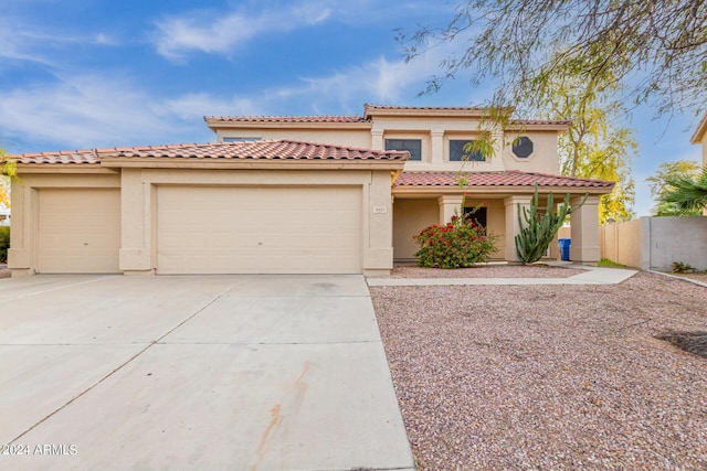 mediterranean / spanish home featuring fence, driveway, stucco siding, a garage, and a tiled roof