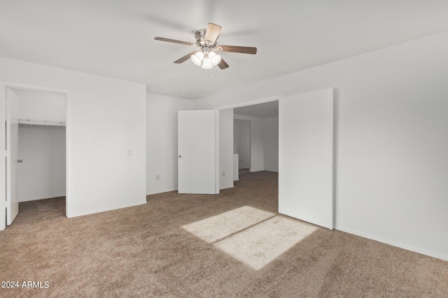 unfurnished bedroom featuring a walk in closet, carpet, a closet, and ceiling fan