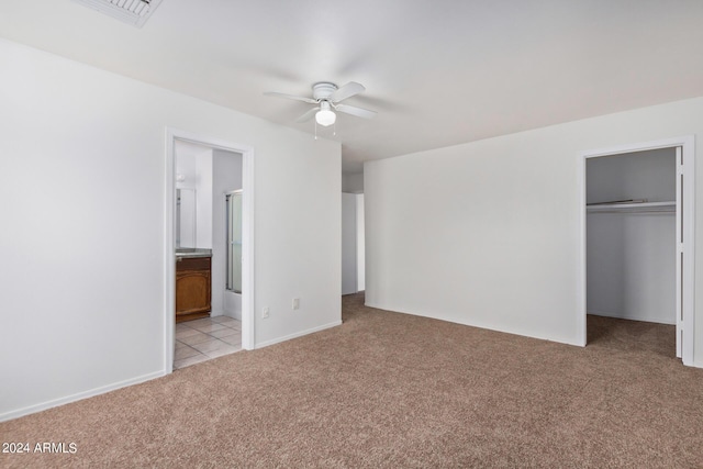 unfurnished bedroom with a ceiling fan, a closet, a walk in closet, light colored carpet, and connected bathroom