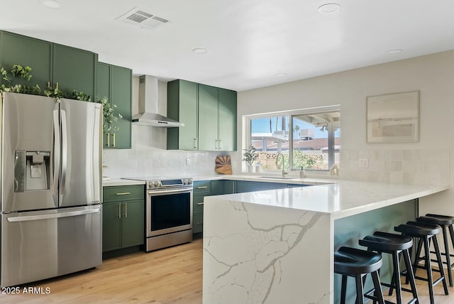 kitchen with wall chimney range hood, a sink, appliances with stainless steel finishes, green cabinets, and a peninsula
