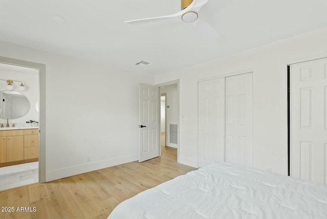 bedroom featuring light wood-style floors, ensuite bathroom, a sink, baseboards, and a ceiling fan
