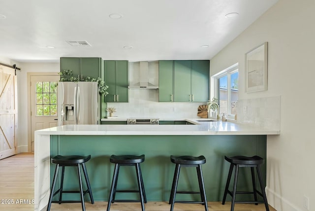 kitchen featuring a barn door, stainless steel appliances, wall chimney exhaust hood, visible vents, and green cabinetry