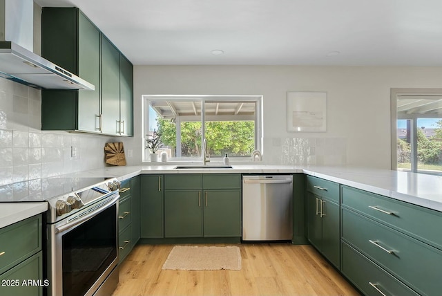 kitchen with wall chimney range hood, a sink, green cabinets, and stainless steel appliances