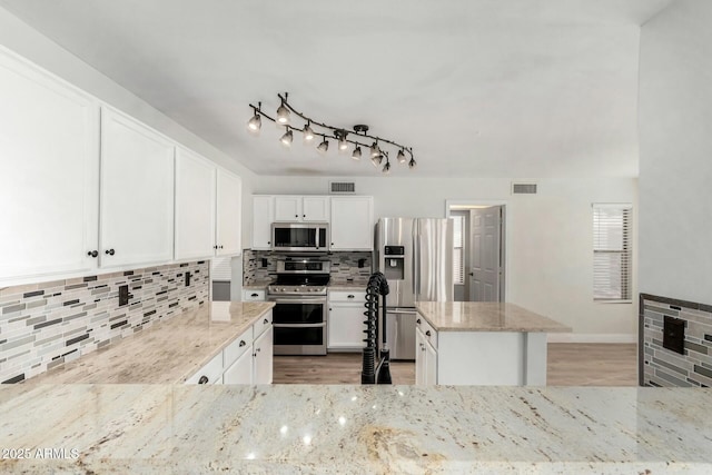 kitchen with stainless steel appliances, light stone countertops, white cabinets, and decorative backsplash